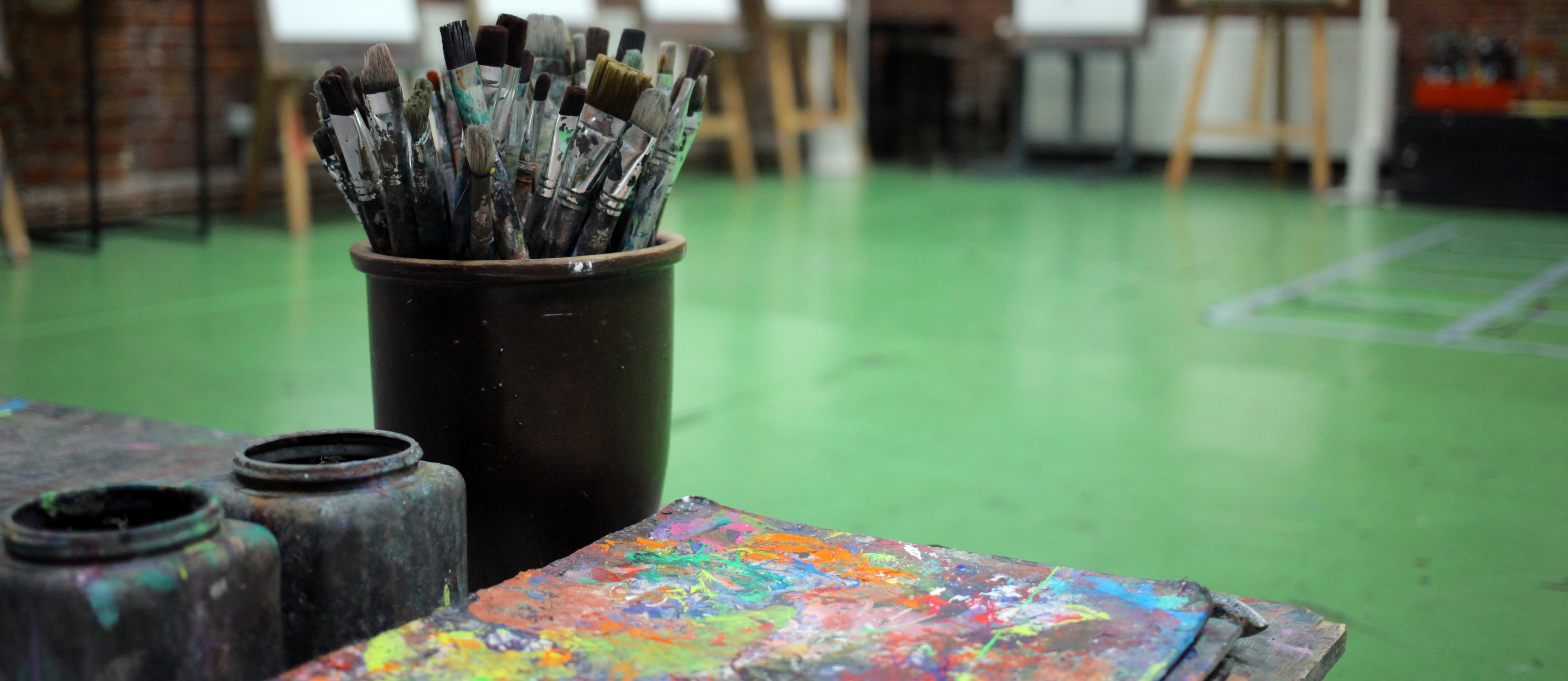 Pinseltopf und Farbpalette im Atelier, Staffeleien unscharf im Hintergrund