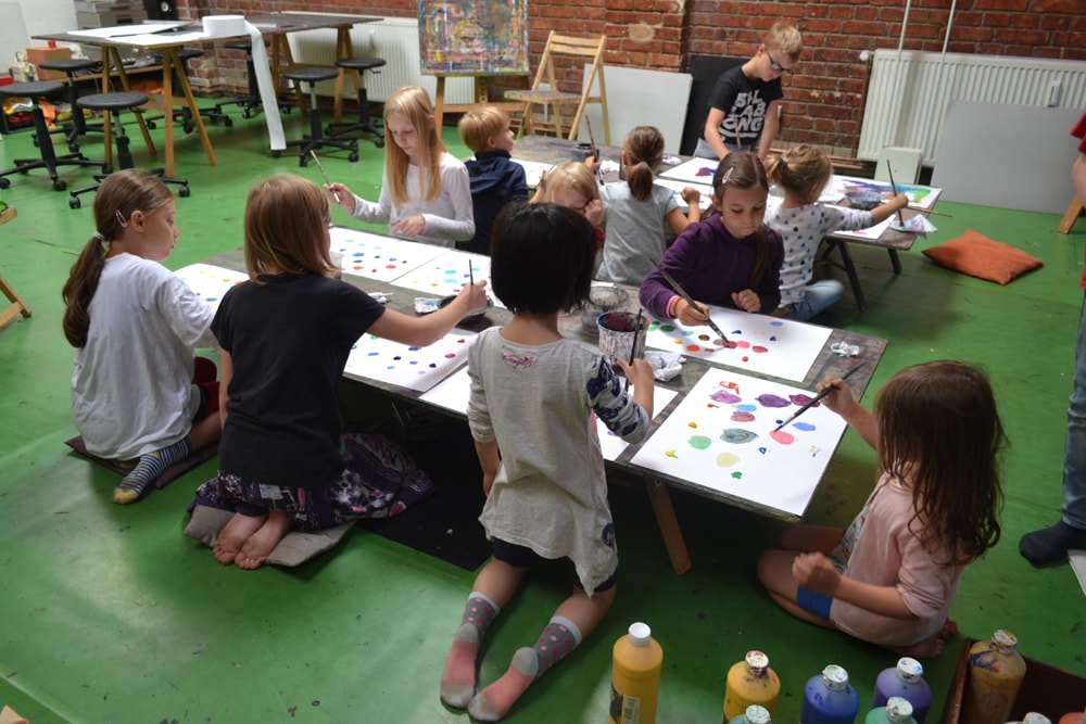 Kinder malen auf dem Boden des Ateliers mit Farbtöpfen